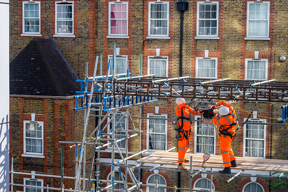 man wearing orange high visibilty workwear suspended from ropes working at extreme heights